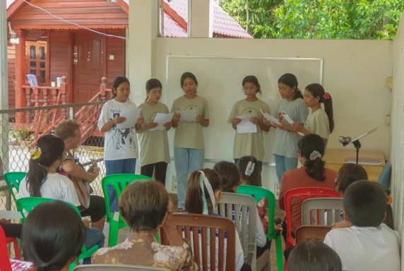 Sechs Jugendliche stehen vor einer Gruppe und präsentieren etwas in einem Raum.